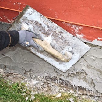 Reparere grunnmur: Første lag røres opp til en grøtaktig konsistens og kastes på med en murskje Reparere grunnmur: Første lag røres opp til en grøtaktig konsistens og kastes på med en murskje